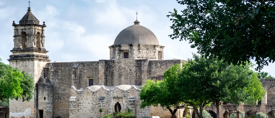 Mission San Jose in San Antonio, its bell tower and dome above stone walls and green trees