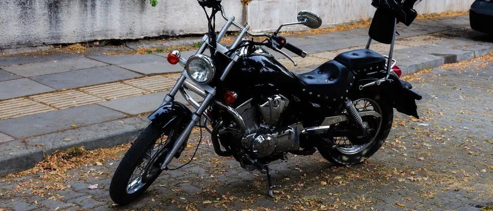 A black cruiser motorcycle parked at the kerb of a paved street beside a low wall