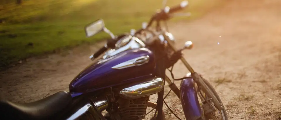 The purple fuel tank and chrome of a parked cruiser motorcycle on a dirt track in warm evening light