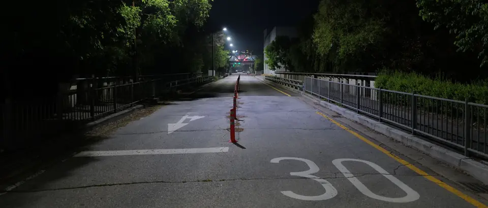 An empty two-lane street at night under bright streetlights, with a row of lane-divider posts down the middle